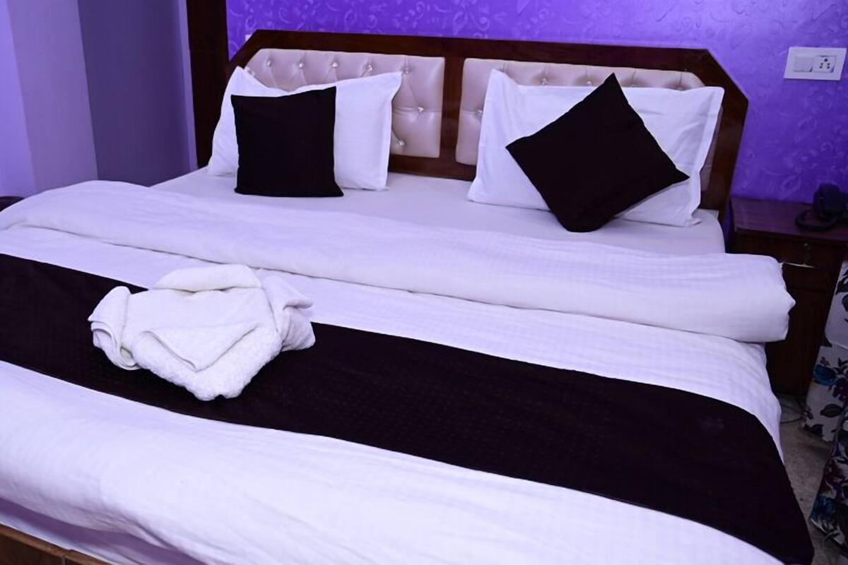A neatly made bed with white and black bedding, a folded towel, and a wooden headboard.