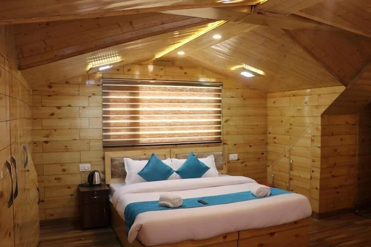 A wooden cabin room with a bed, a nightstand, and a window with blinds.
