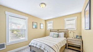 A bedroom with a bed, bedside tables, and windows with blinds.