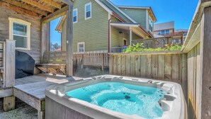 A hot tub in a backyard with wooden deck and a house in the background.