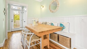 A dining area with a wooden table and white chairs, a bench with cushions, and a wall-mounted mirror.