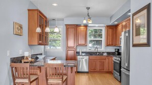 A modern kitchen with wooden cabinets, a stainless steel refrigerator, a dishwasher, and a large window providing natural light. - Infinity View - Ocean Front (Lincoln City)