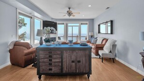 A spacious living room with a large wooden cabinet, a brown leather sofa, a grey armchair, and a view of the ocean through large windows. - Infinity View - Ocean Front (Lincoln City)