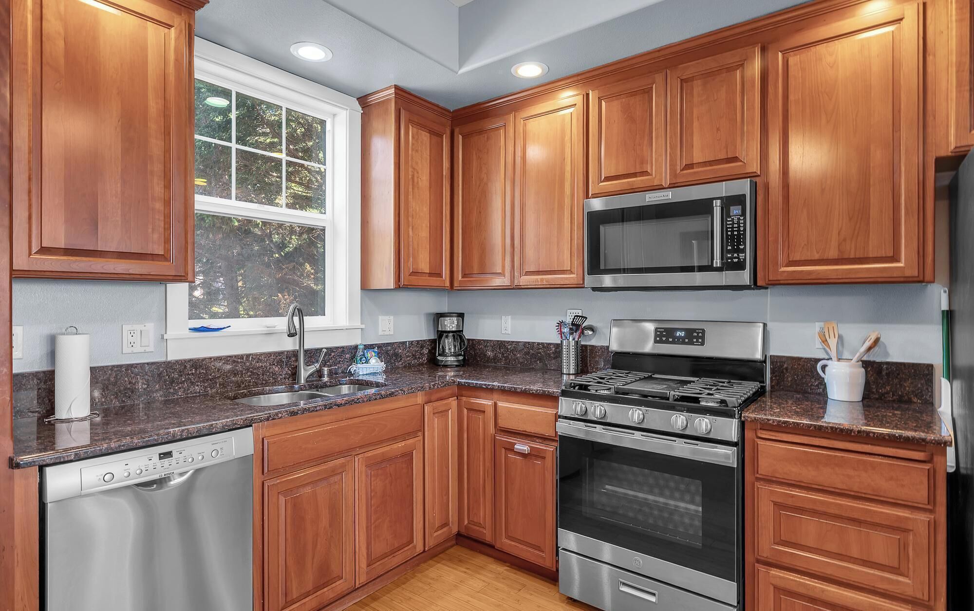 A modern kitchen with wooden cabinets, a Bosch dishwasher, a stainless steel stove, and a microwave.