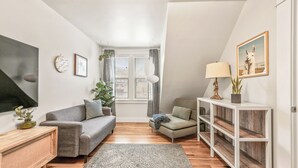Una sala de estar moderna con un sofá gris, una mesita de madera, un tapete estampado y una consola blanca con una lámpara.