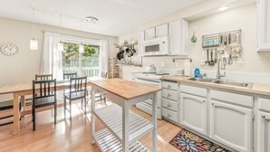 A modern kitchen with white cabinets, a wooden dining table, and a large window. - Surf Song - Walk to the Beach (Lincoln City)