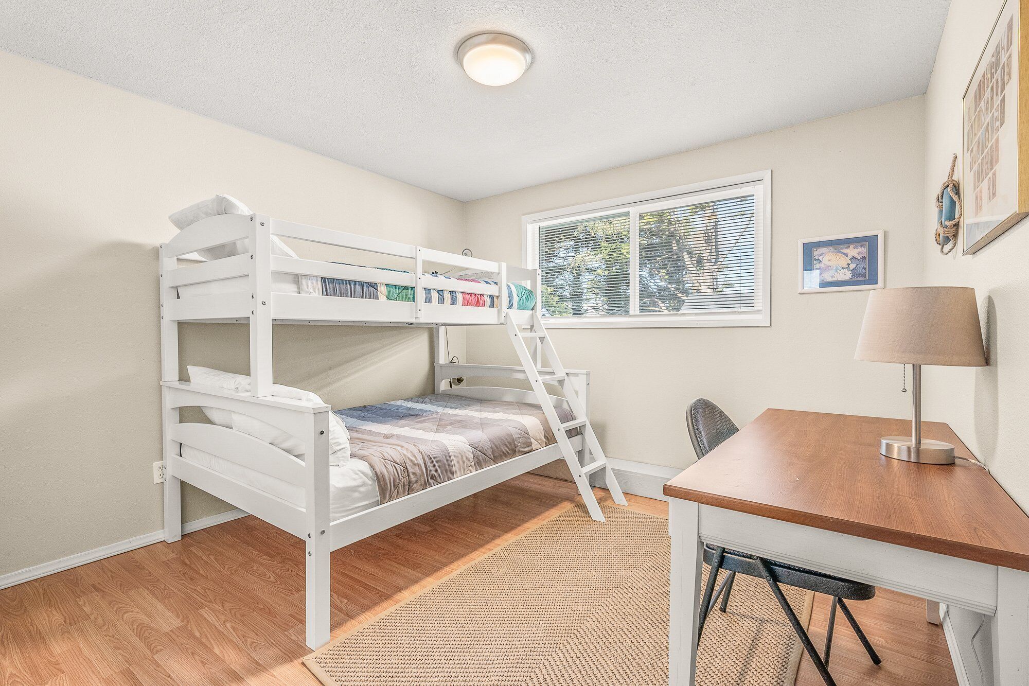 A room with a bunk bed, a desk, a chair, a lamp, and a window with blinds.