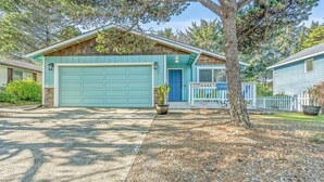 A two-story house with a blue garage door, a front porch with a white picket fence, and a 'Warning' sign. - Surf Song - Walk to the Beach (Lincoln City)