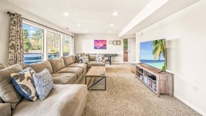 A living room with a beige sofa, a coffee table, a TV, and a bookshelf. - The Flip Flop Inn - Walk to the Beach (Lincoln City)