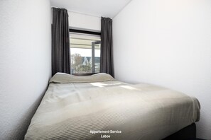 Una cama individual en una habitación con ventana, cortinas y vistas a edificios.