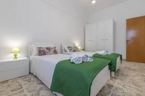 Ein Hotelzimmer mit zwei Betten, weißer Bettwäsche, grünen Zudecken, einer Holztür und einem Marmorboden.