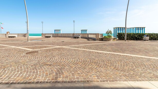Een verharde promenade met uitzicht op zee, bankjes en een blauw-gestreept gebouw met de naam 'Annite'.