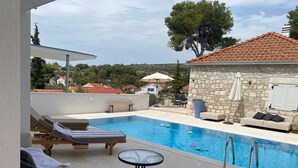A pool area with lounge chairs, a table, and a stone building with a tiled roof. - Exclusive Holiday Home Villa Marumare (Hvar)
