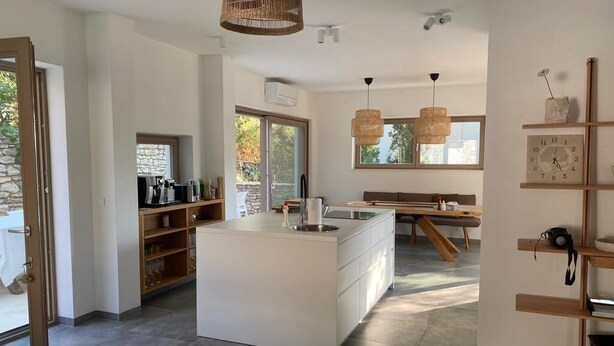 A modern kitchen with a central island, wooden shelves, and pendant lighting. - Exclusive Holiday Home Villa Marumare (Hvar)
