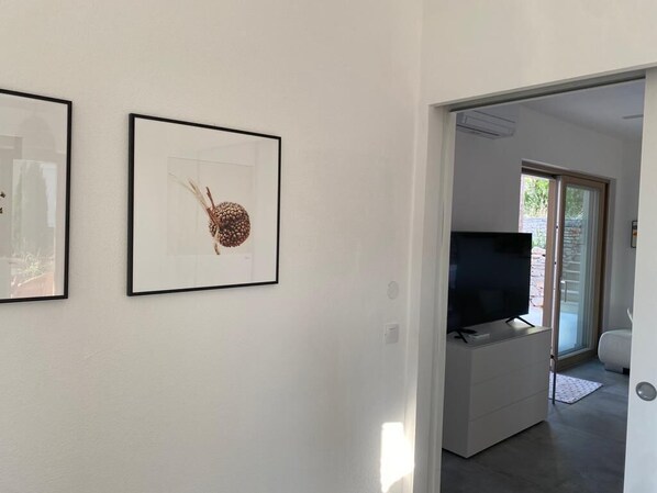 A hallway with framed artwork on the wall, a television in a white entertainment unit, and a door leading to another room. - Exclusive Holiday Home Villa Marumare (Hvar)