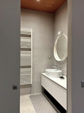 Un baño moderno con tocador blanco, un espejo redondo y un perchero para toallas.