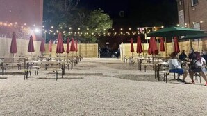An outdoor seating area with tables and chairs, covered by red umbrellas, and string lights in the background. - Sun-Drenched Apartment in City Unit B (Baltimore)