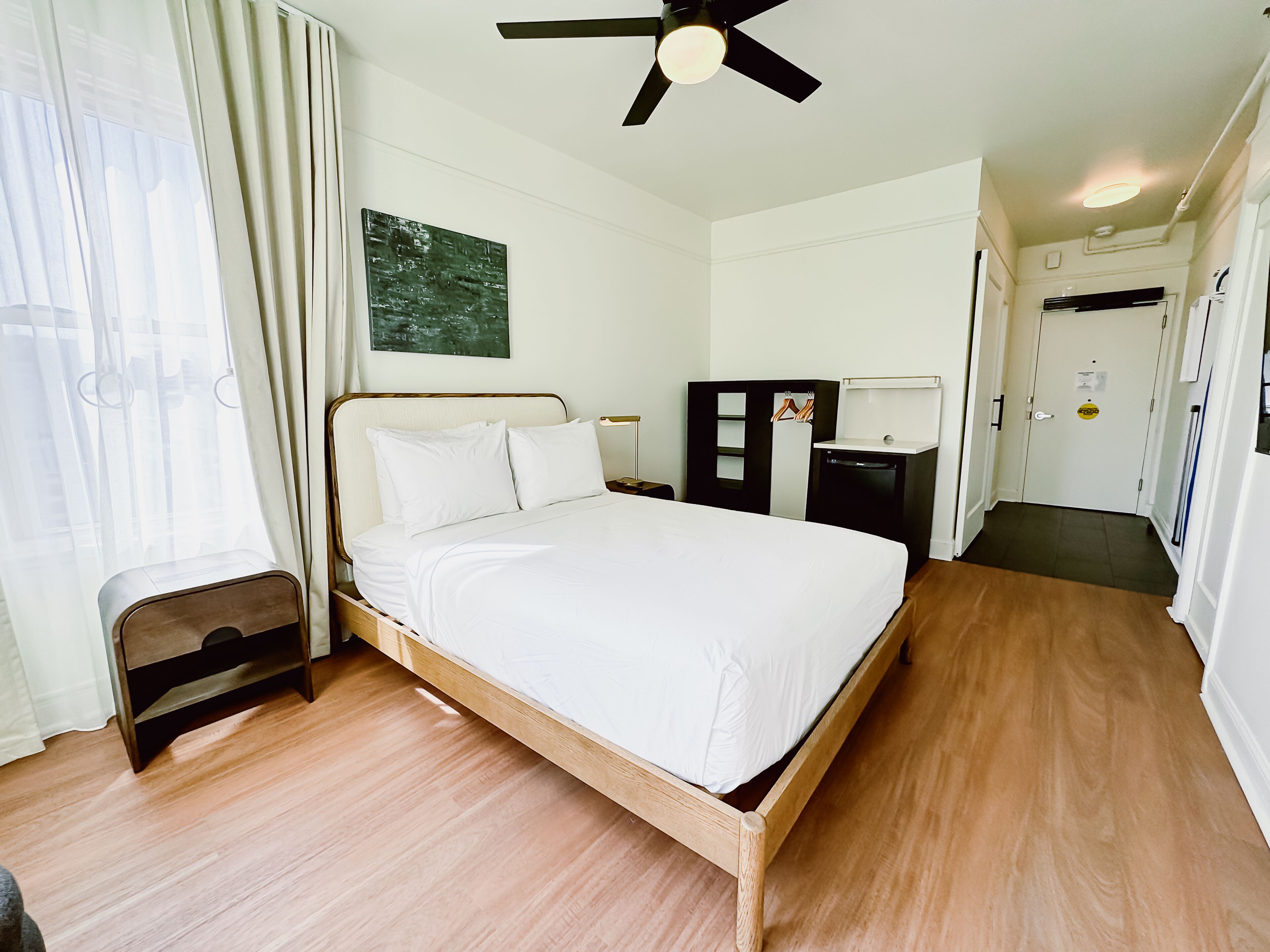 A neatly arranged bedroom with a wooden bed, a ceiling fan, a small bedside table, and a wardrobe.