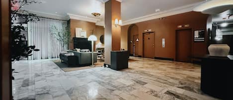 A spacious lobby with a marble floor, a seating area with sofas, and a reception desk.