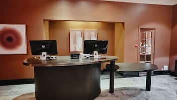 A reception desk with two monitors, a telephone, and a small printer. There is a marble floor and a door with a glass panel in the background.