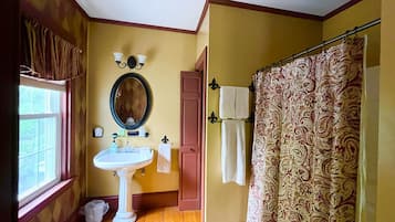 A bathroom with a pedestal sink, a mirror, a shower curtain, and a window with curtains.