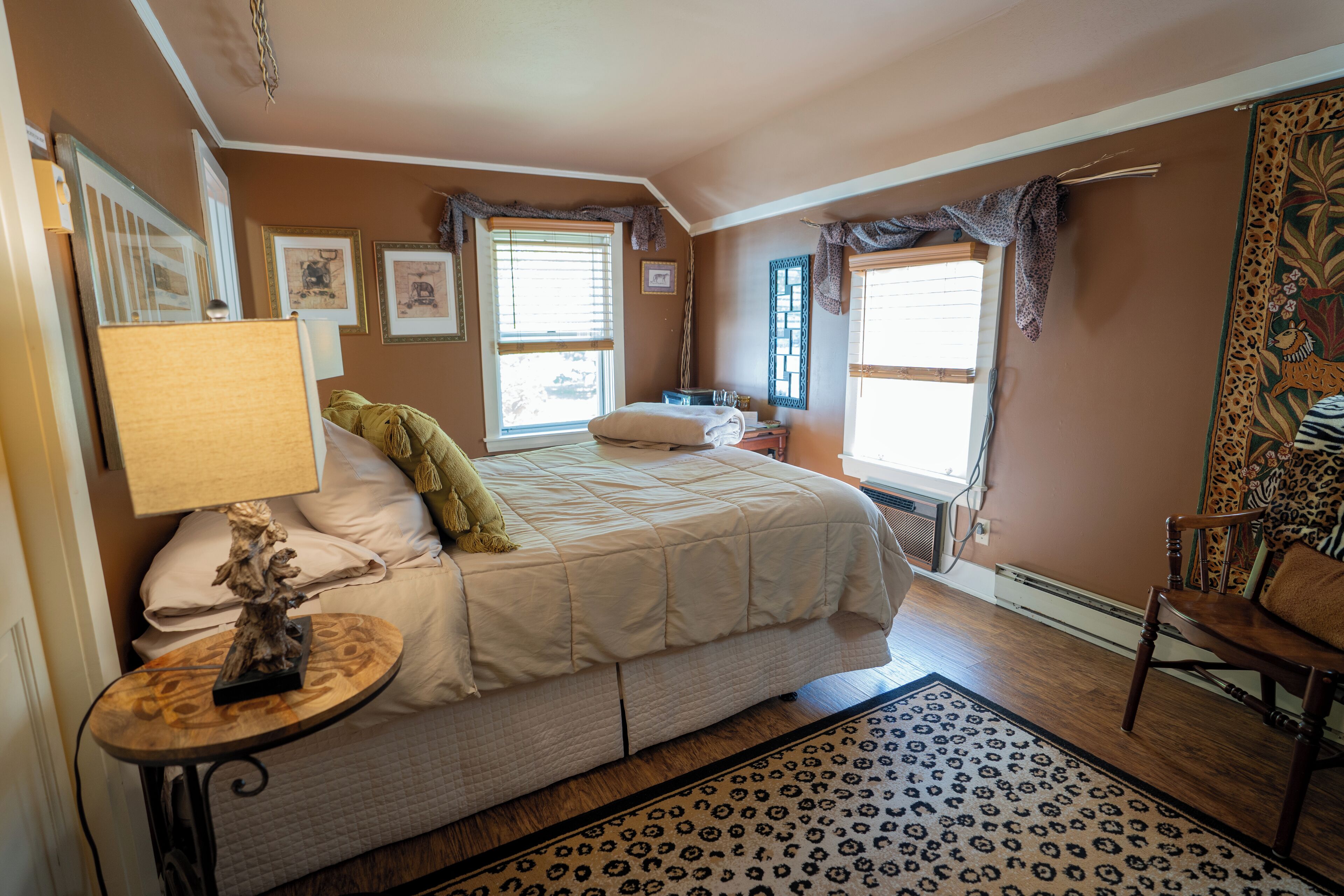 A bedroom with a bed, a nightstand, a lamp, a chair, and a patterned rug.