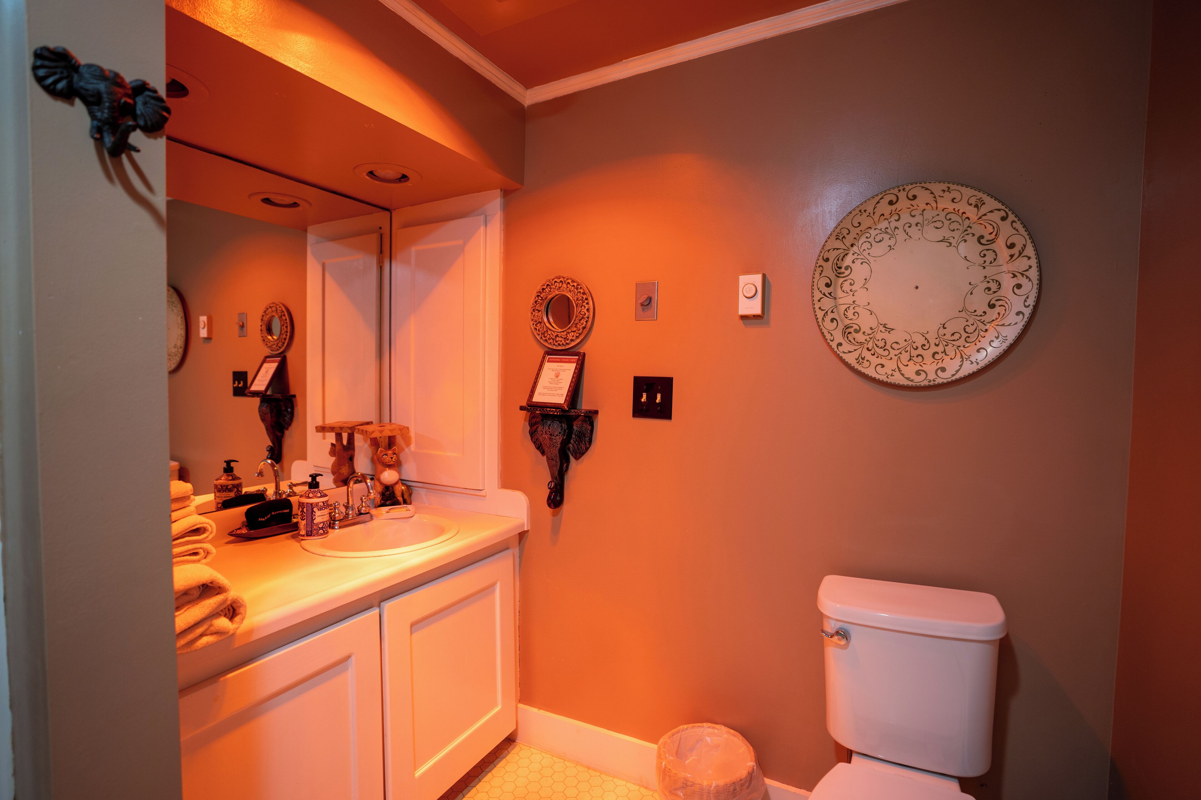 A bathroom with a white sink, mirror, and toilet. There are decorative plates on the wall and a towel rack.