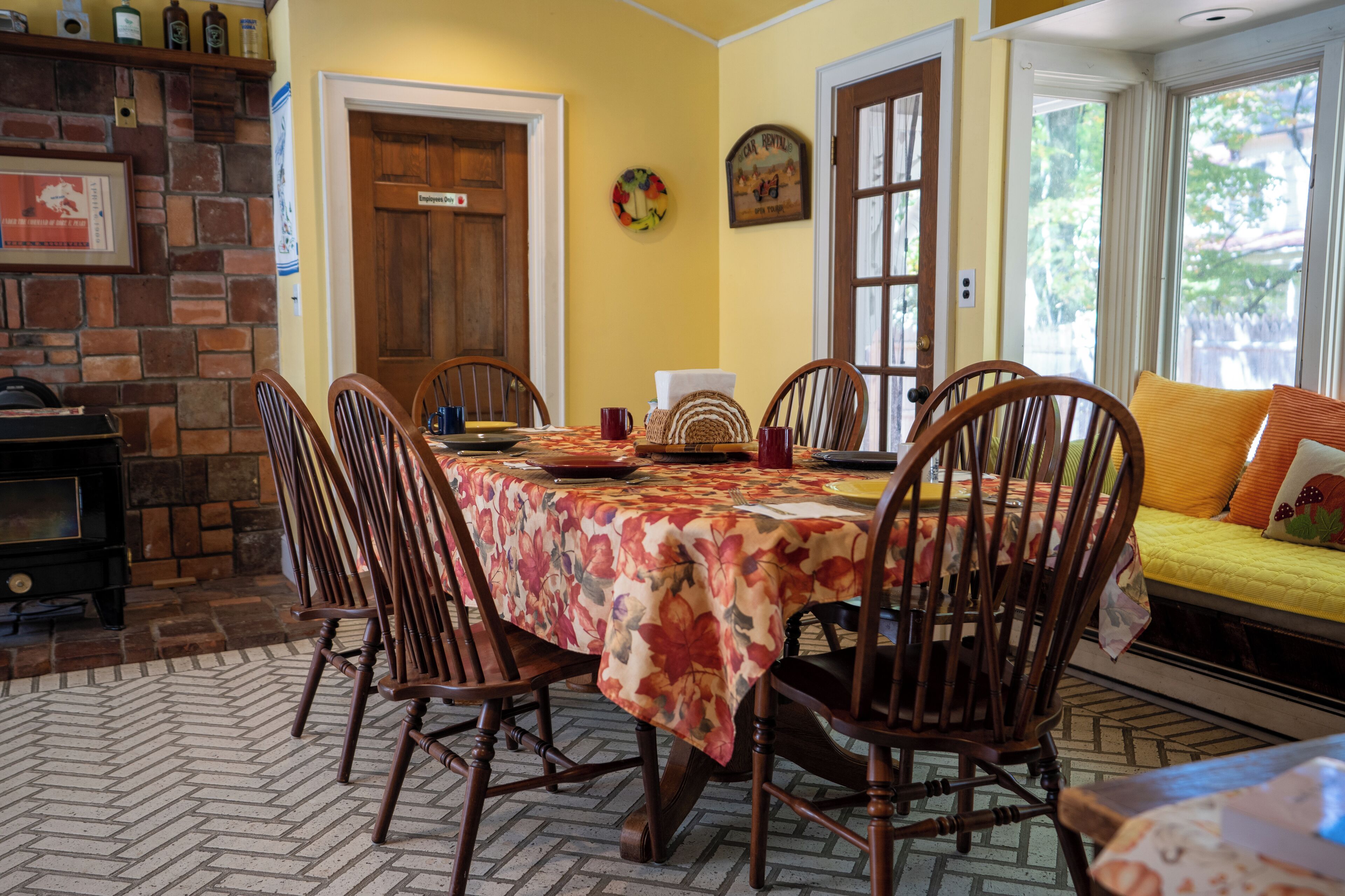 A dining area with a round table covered in a floral tablecloth, surrounded by wooden chairs.