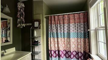 Un baño con inodoro blanco, lavamanos, espejo, cortina de ducha estampada con motivos geométricos y una lámpara colgante.