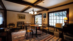 A dining area with a wooden table, chairs, and a patterned rug. There is a window with a view of a building, a hanging light fixture, and a sign on the wall. - Admiral Peary Inn (Fryeburg)