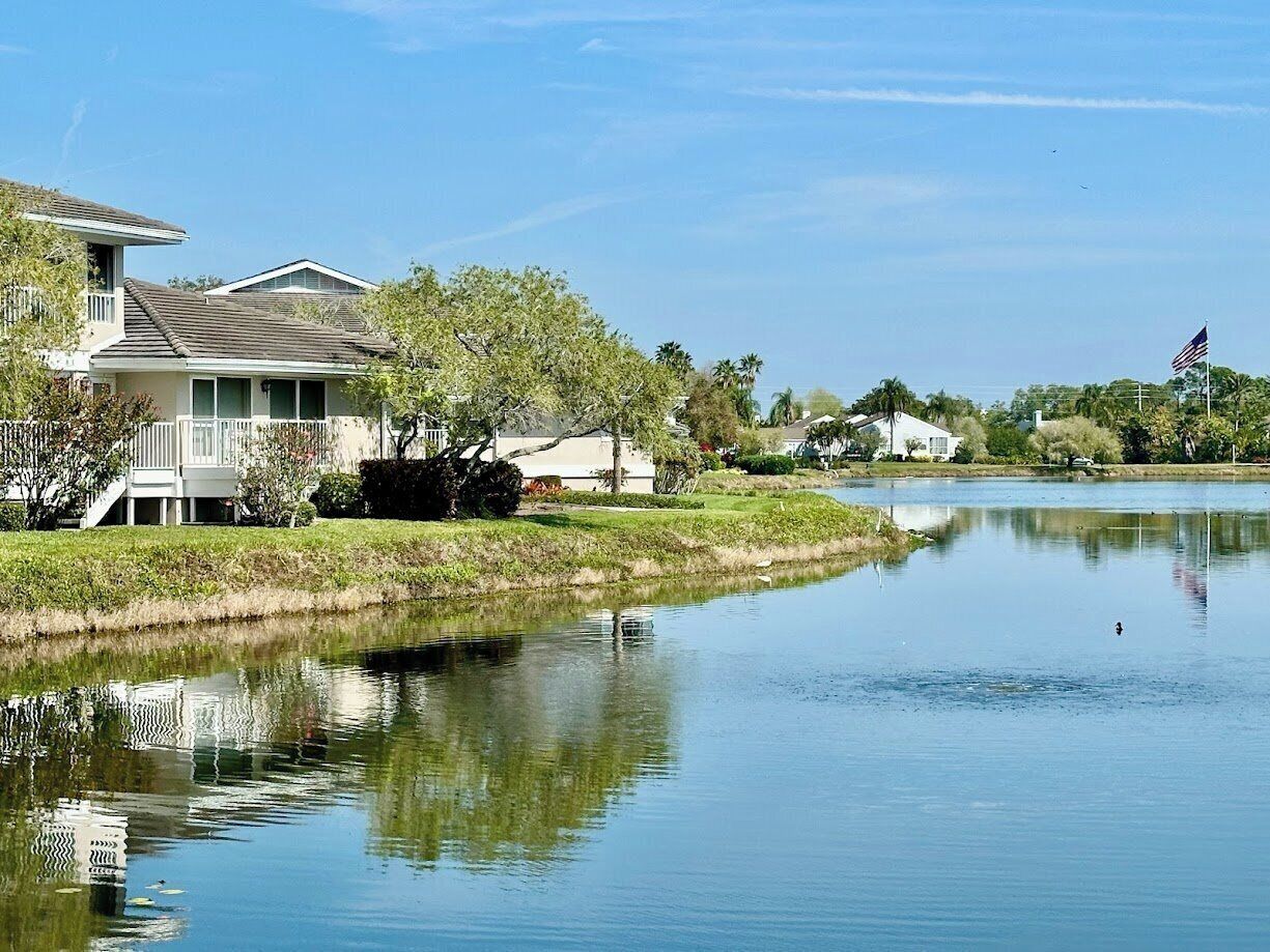 A calm lake with a house on the left and a flag on the right.