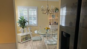 A dining area with a glass table, white chairs, a chandelier, and a potted plant.