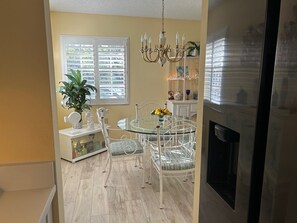 A dining area with a glass table, white chairs, a chandelier, and a potted plant.