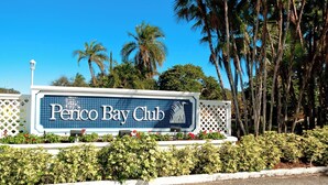 A sign for the Penico Bay Club with a clear view of the surrounding greenery and palm trees.