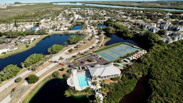 An aerial view of a residential area with multiple lakes, a tennis court, and a swimming pool.