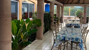 An outdoor patio with tiled flooring, wooden chairs, and tables covered with floral tablecloths. - Hotel Yauco (Rosario)