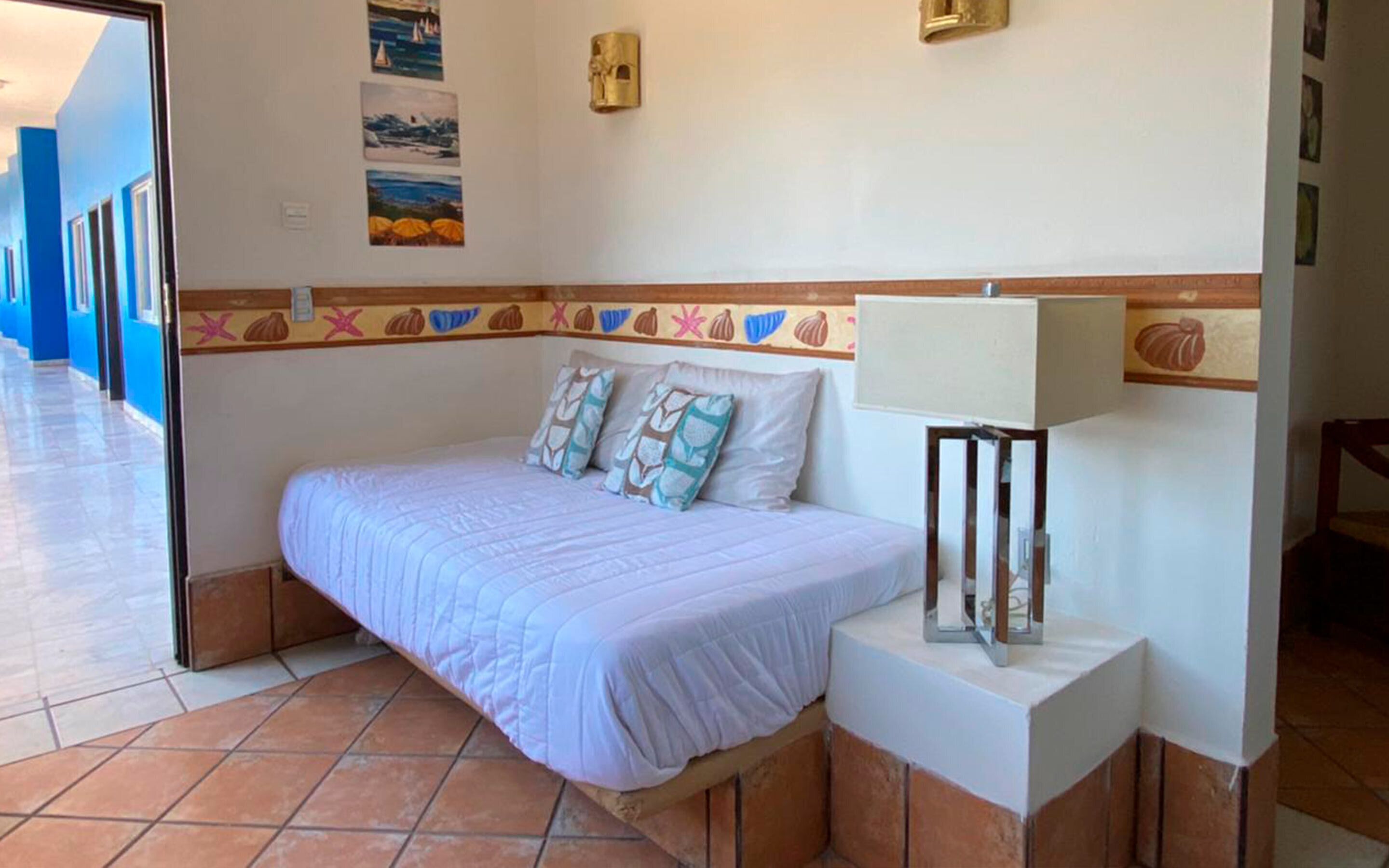 A bedroom with a bed, pillows, a nightstand, a lamp, and a wall with decorative tiles and paintings.
