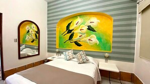 A hotel room with a bed, a bedside table, a mirror, and a wall with a painting. - Hotel Yauco (Rosario)