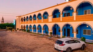 A hotel with a row of blue arched windows and a white car parked in front. - Hotel Yauco (Rosario)