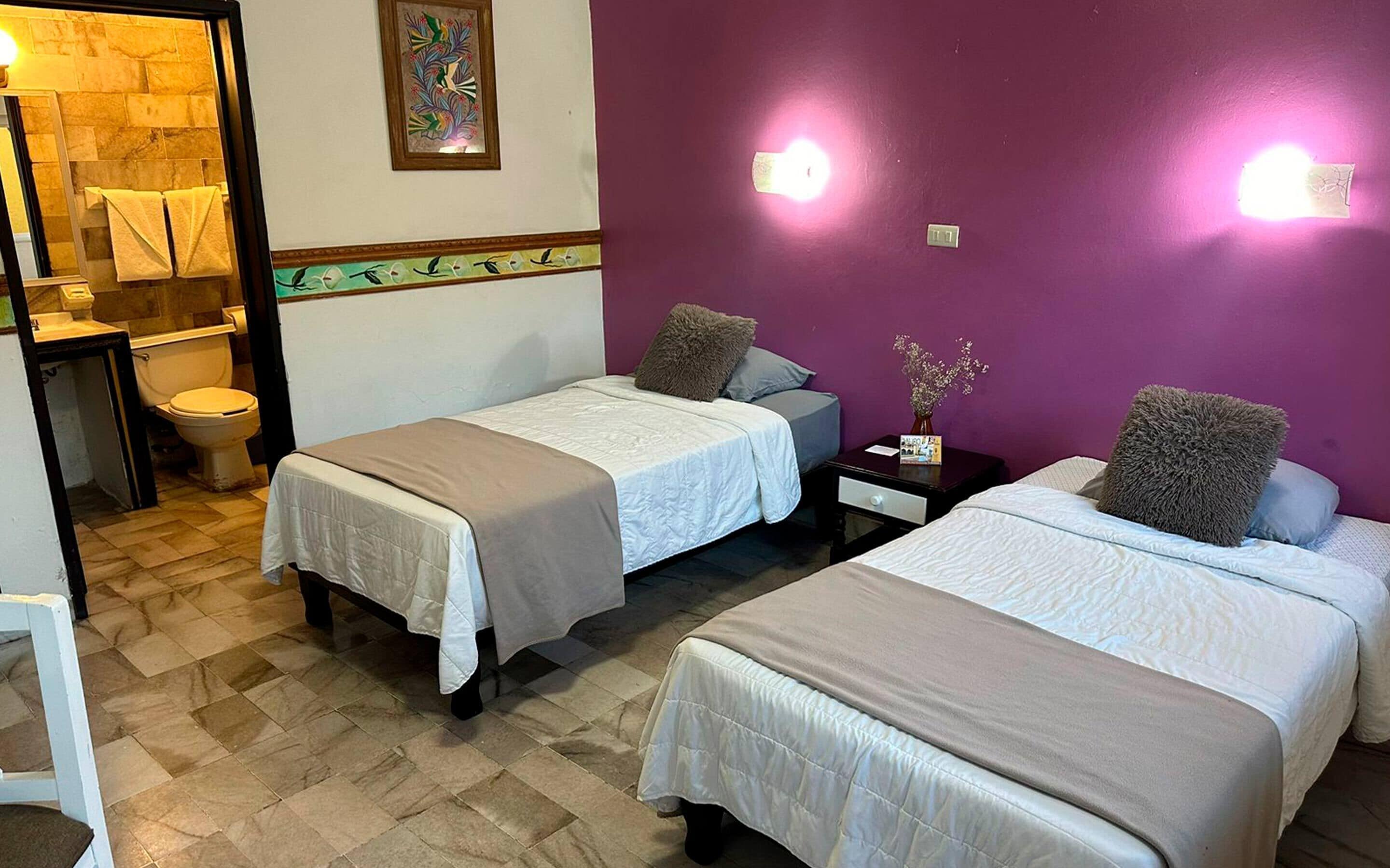 A room with two beds, a bathroom, and a small table with a vase.