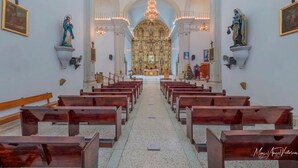 A church interior with pews arranged in rows, a central altar, and statues on the walls. - Hotel Yauco (Rosario)