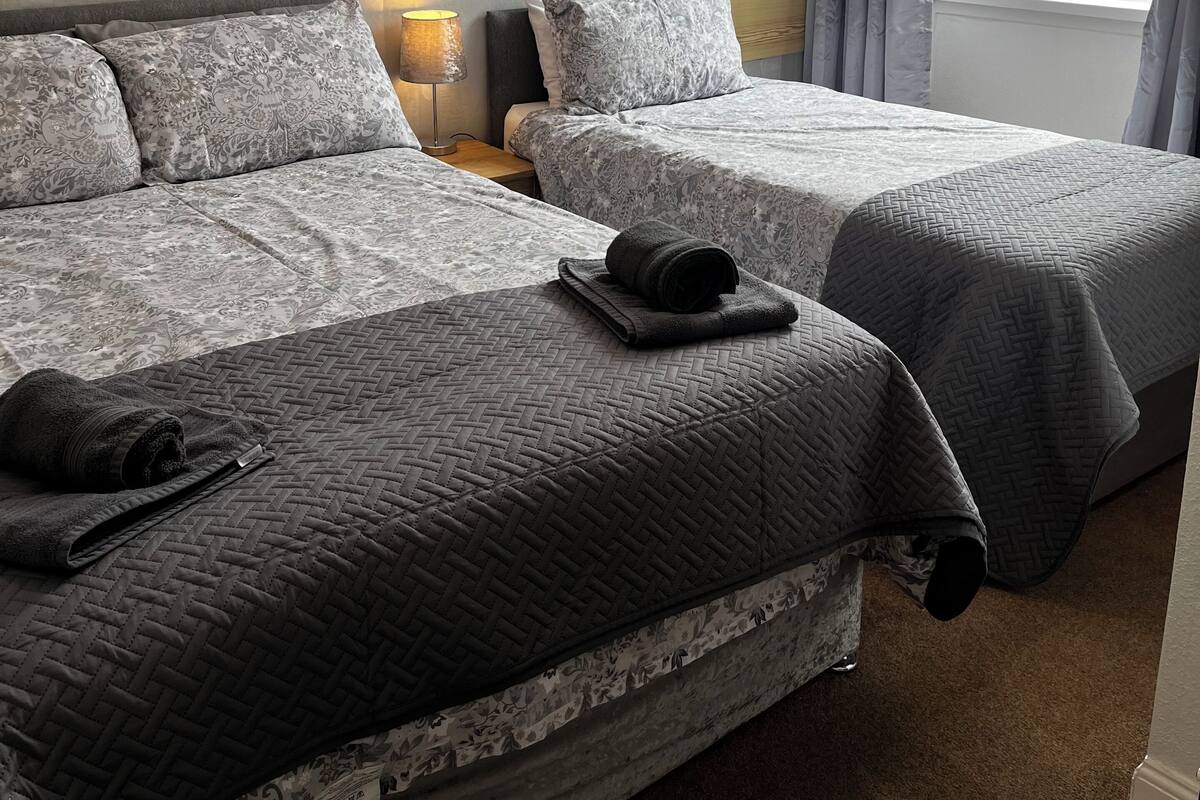 A hotel room with two beds, a nightstand, a lamp, and a window with curtains.