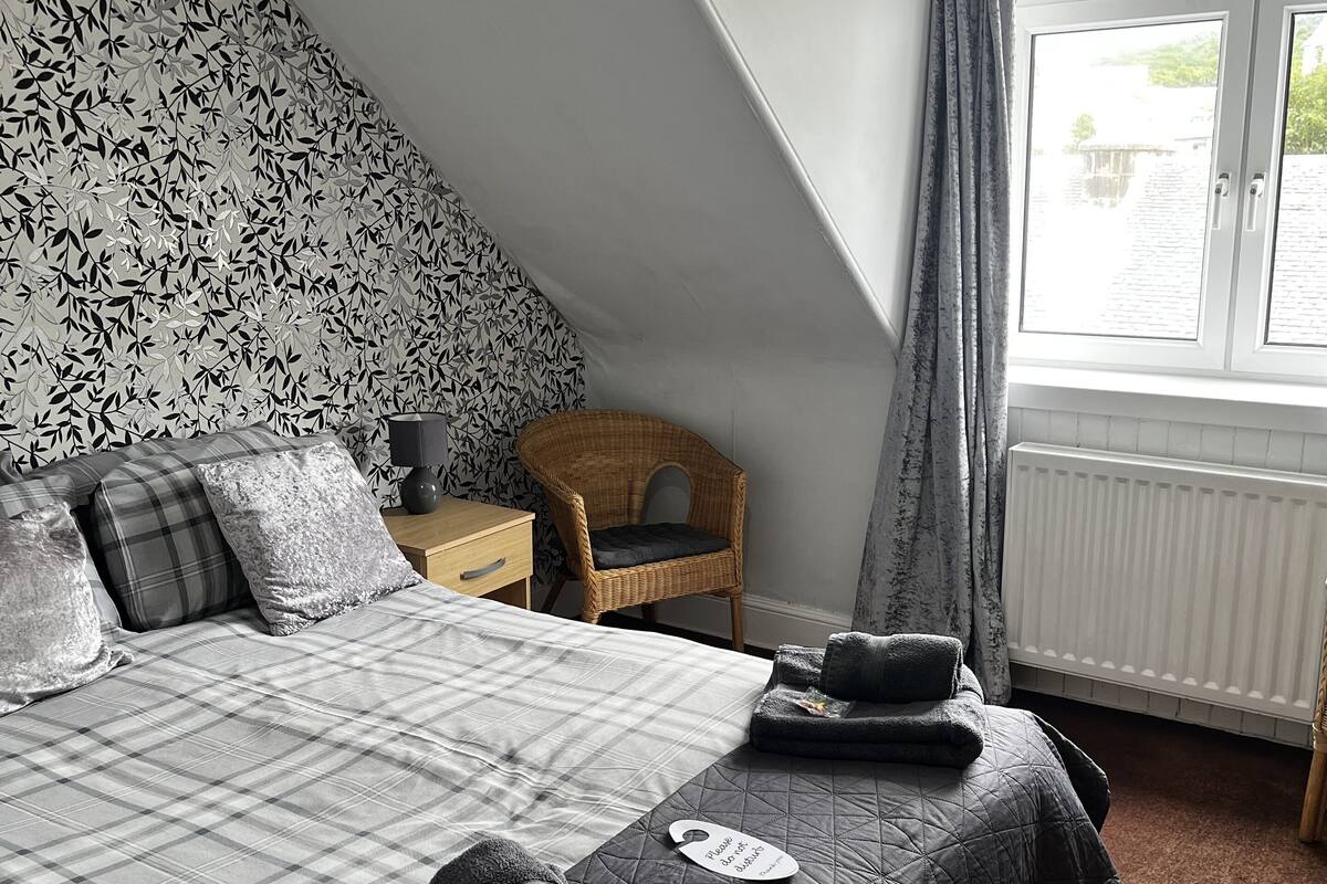 A bedroom with a bed, a chair, a window, and a radiator.