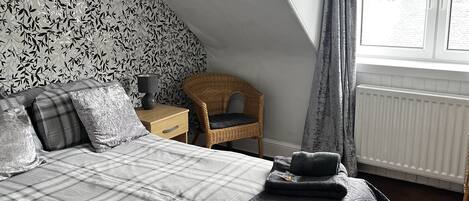 Un dormitorio con cama, una silla, un ventanal y un radiador.