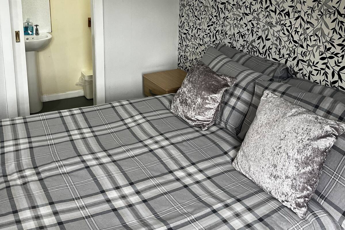A bedroom with a bed, a nightstand, a mirror, and a bathroom visible through an open door.