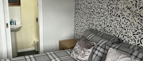 A bedroom with a bed, a nightstand, a mirror, and a bathroom visible through an open door.
