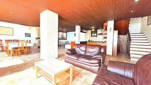 A spacious living area with a brown leather sofa, a wooden coffee table, and a dining table with chairs. A kitchen is visible in the background, and a staircase leads to another level. - Amazing View Costa Brava (Lloret de Mar)