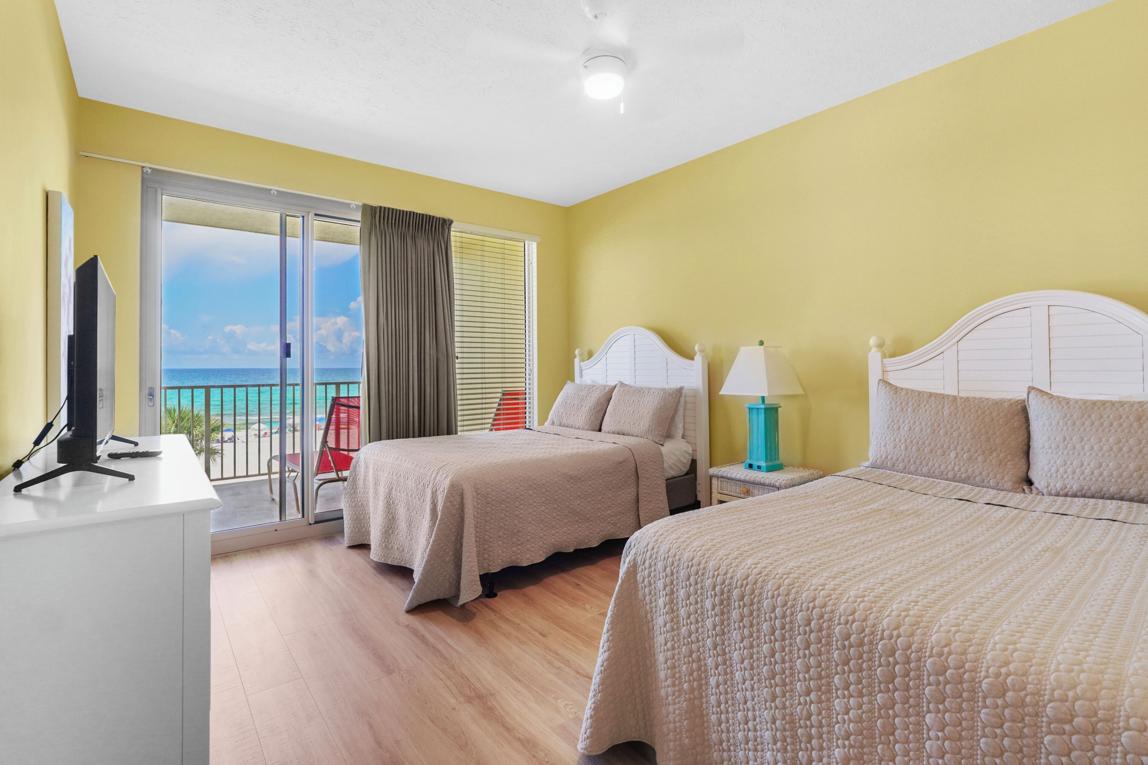A hotel room with two beds, a desk, and a view of the beach.