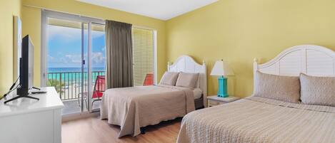 A hotel room with two beds, a desk, and a view of the beach.