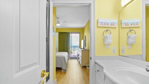 Habitación de hotel con cama, baño con espejo grande y vista a la playa por la ventana.